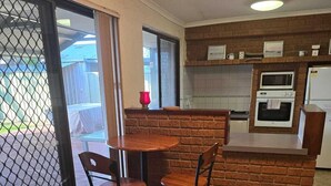 Una cocina funcional con protector mural de ladrillo, microondas y refrigerador. Cuenta con un pequeño comedor con dos sillas y una mesa.