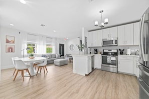 A modern kitchen with white cabinetry, stainless steel appliances, and a dining area with a round table and chairs.