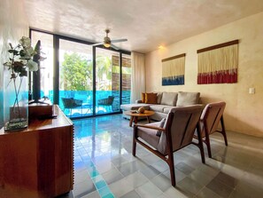 A spacious living room with a sofa, chairs, a coffee table, and a view of a swimming pool through large glass doors. - Sabor a Miel – Duplex near beach with pool & gym (Playa del Carmen)