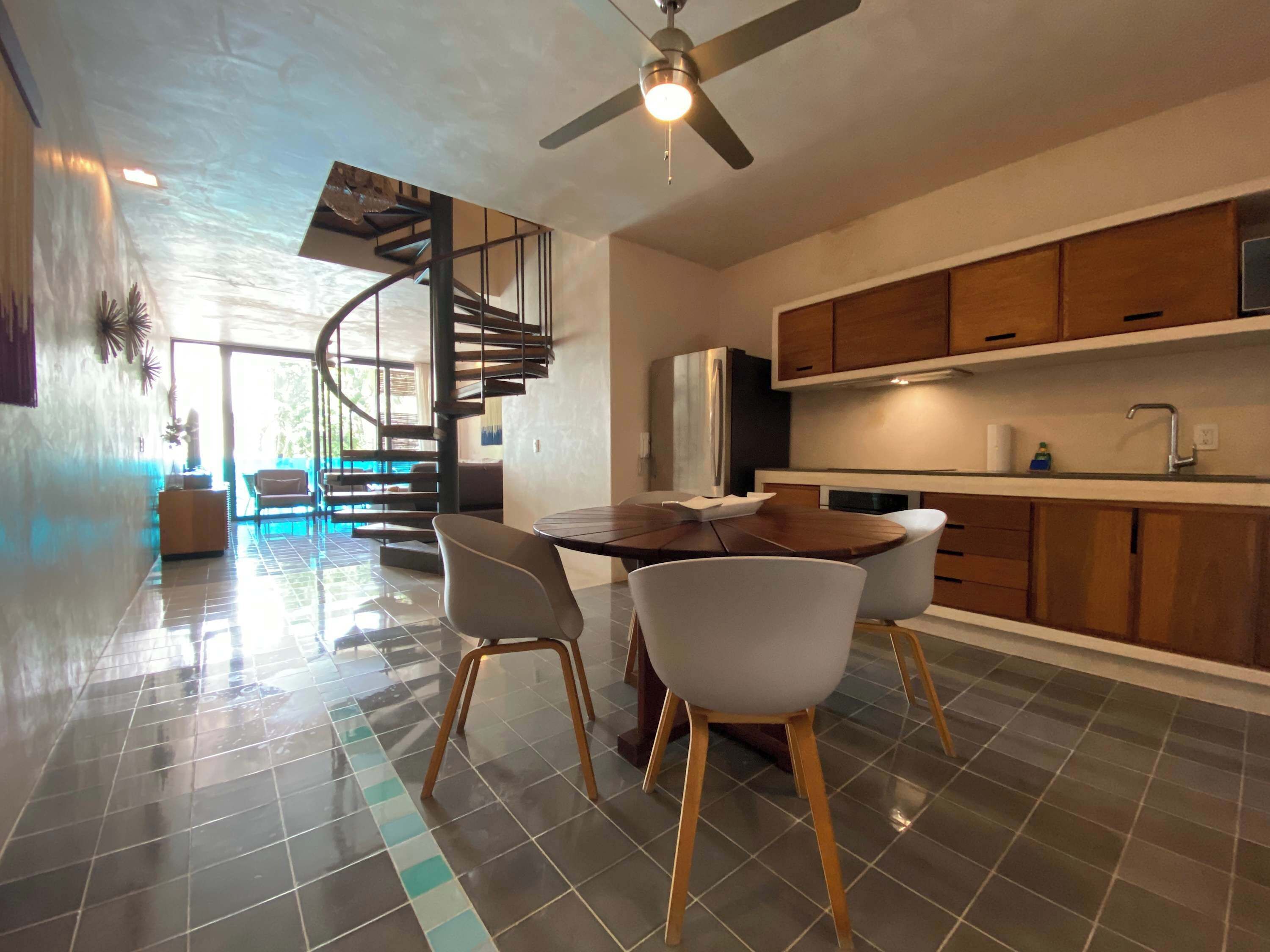 A modern kitchen with wooden cabinets, a built-in oven, and a dining area with a round table and chairs.