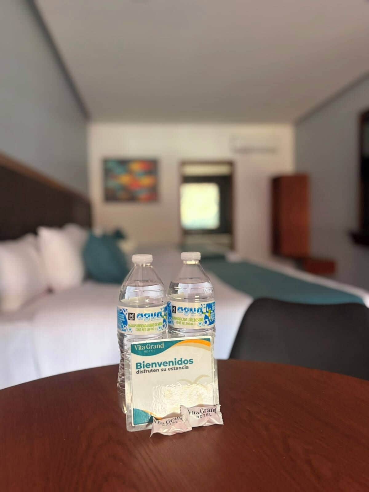 A hotel room with a bed, a desk, and two bottles of water on a table.