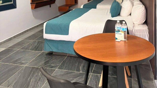 A hotel room with a bed, a round wooden table, a chair, a TV, a wardrobe, and a painting on the wall. - Vita Grand Hotel  (Nuevo Nayarit)