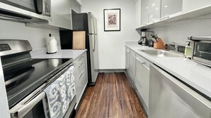 A modern kitchen with stainless steel appliances, a wooden cutting board, and a framed artwork on the wall. - Luxury 2BR/1BA - 10 min to NYC (Hoboken)