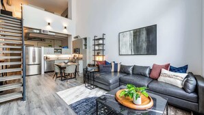 Un salon moderne avec un canapé d’angle, une table basse agrémentée d’une plante, et une cuisine en arrière-plan.