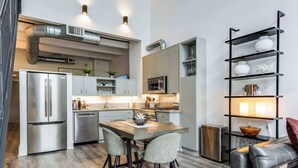 Une cuisine moderne dotée d’appareils électroménagers en acier inoxydable, un coin repas avec une table et des chaises en bois, et une étagère noire agrémentée d’objets décoratifs.