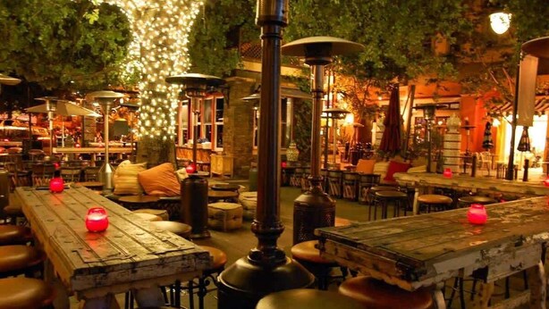 Un espace de restauration en plein air avec des tables et des bancs en bois rustique, des guirlandes lumineuses et une atmosphère chaleureuse.