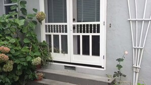 Una casa de fachada gris, con puertas dobles blancas y una barandilla blanca, y un pequeño porche con plantas en macetas.