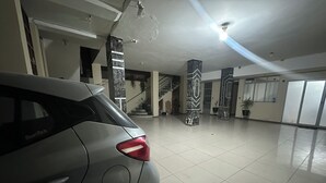 Amplio espacio interior con un automóvil en primer plano, una escalera y pilares decorativos.