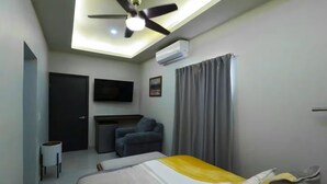 Ein Hotelzimmer mit Bett, Schreibtisch, Stuhl, Deckenventilator, Klimaanlage und Fernseher.