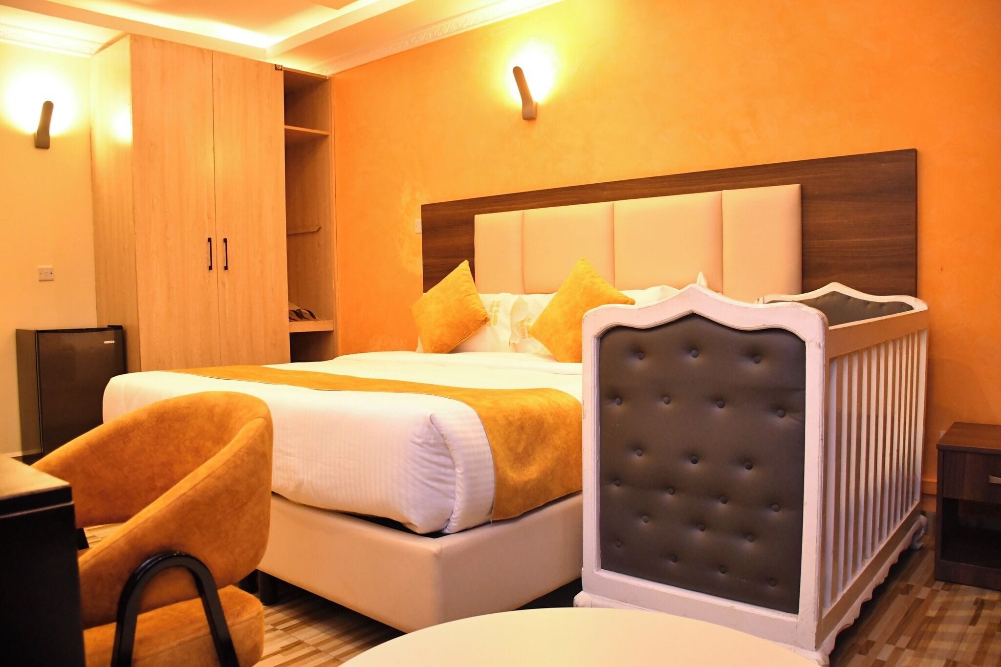 A hotel room with a large bed, a wardrobe, a bedside table, and a chair.