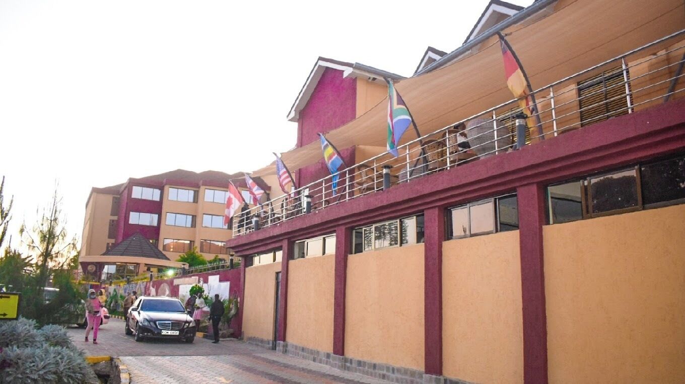A multi-story building with a balcony, flags, and a paved entrance area.