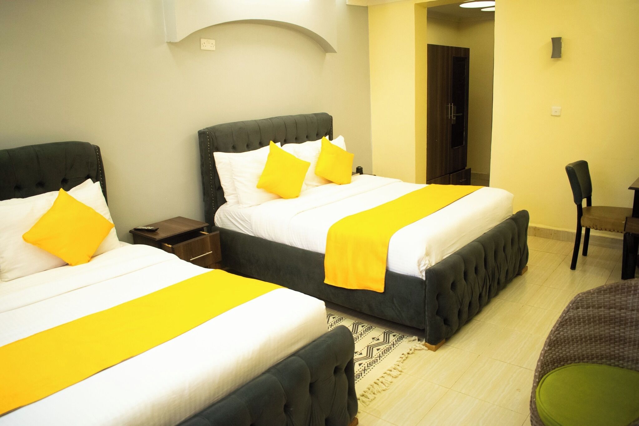 A hotel room with two beds, each with a yellow bedspread and matching pillows. There is a small table and a chair in the room.