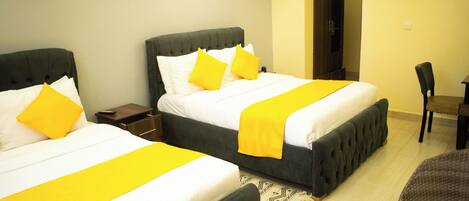 Habitación de hotel con dos camas, cada una con una colcha amarilla y almohadas a juego. Hay una mesita y una silla en la habitación.