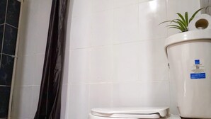 A bathroom with a white toilet, a shower curtain, and a white tiled wall. - Independent room (David)