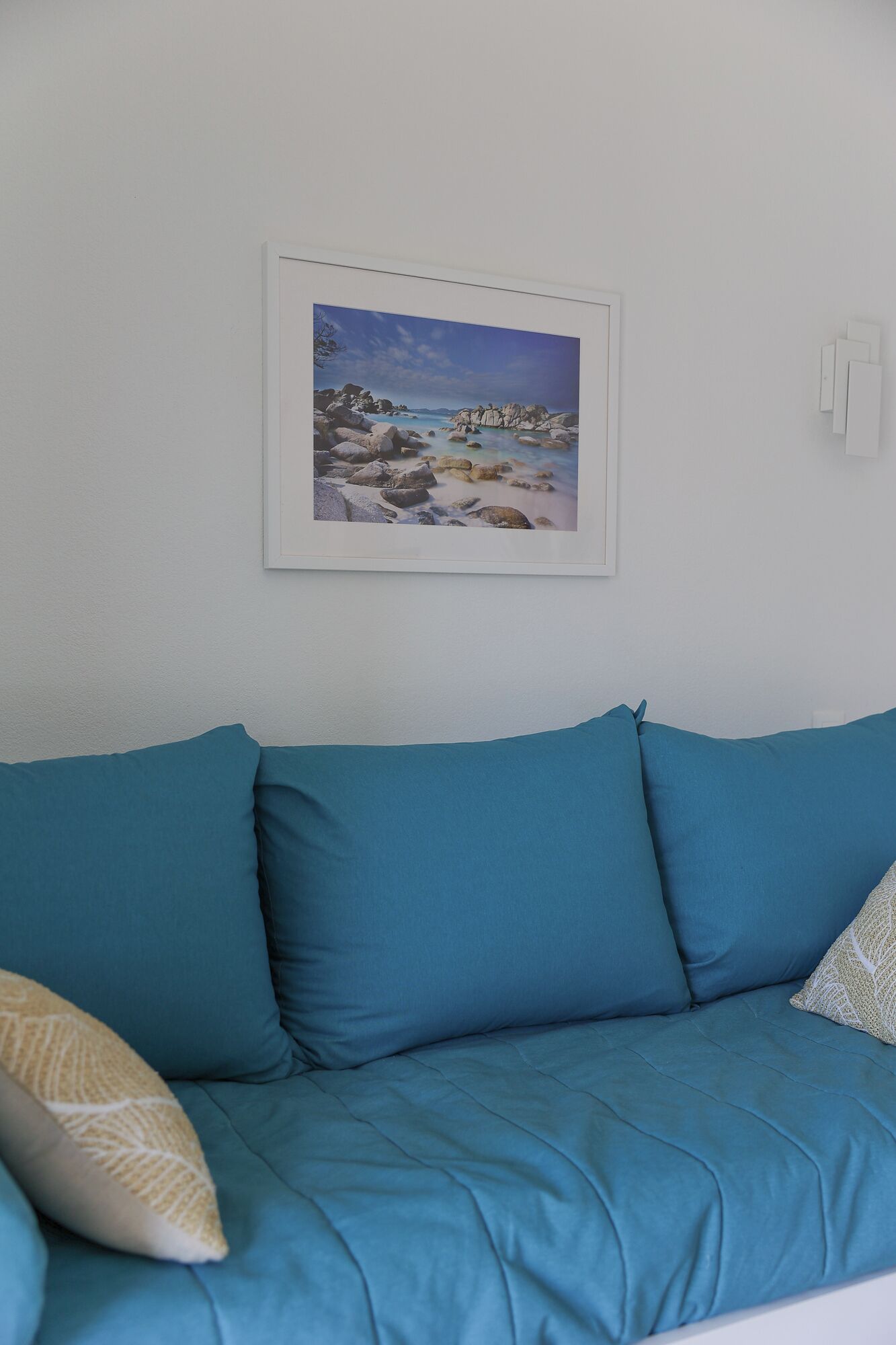 En soffa i turkos färg, och ovanför den hänger ett inramat fotografi som föreställer ett landskap.