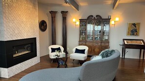 A living room with a fireplace, two white armchairs, a grey sofa, a wooden cabinet with glass doors, and a painting on the wall. - Furnished 30 to 60 day rental - Feb/March - Architectural Gem with Bay Views (Sausalito)