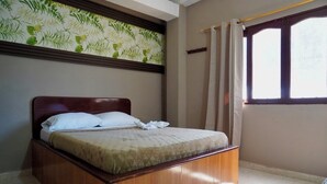 A neatly made bed with a wooden headboard, a window with curtains, and a wall with a leaf-patterned wallpaper. - Hotel Lua (Santa Marta)