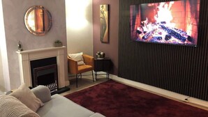 Ett vardagsrum med en öppen spis, en soffa, en tv och en dekorativ spegel.