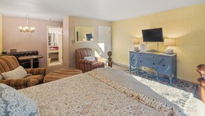 Ein Hotelzimmer mit einem großen Bett, einem Fernseher, einem Schminktisch, einem Sessel und einem kleinen Tisch.