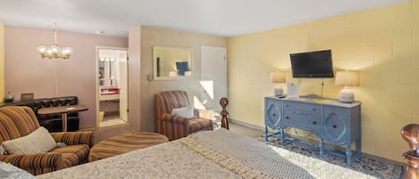 Una habitación de hotel con una cama grande, televisión, cómoda, silla y una mesita.