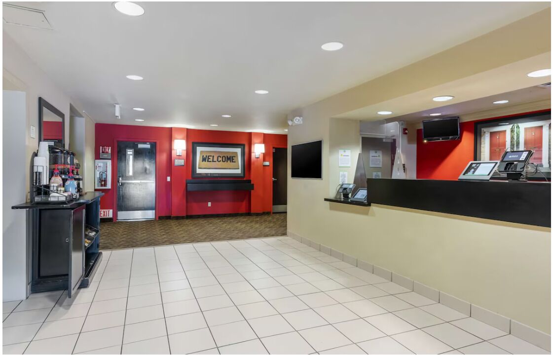 A reception area with a red wall, a welcome sign, a reception desk, a coffee machine, and a TV screen.