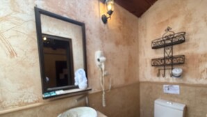 Un baño con lavamanos de mármol, inodoro, espejo y lámpara de pared.