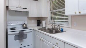 A kitchen with white cabinets, a stove, a sink, and a window with blinds. - Charlotte International Villa 1 Bed-A2 (Charlotte)