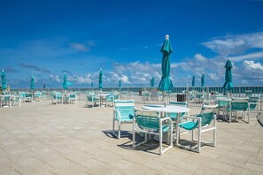 A rooftop terrace with outdoor seating and umbrellas, overlooking a body of water. - Oceanview Condo on No-Drive Beach | Balcony, Pool, Peaceful Escape (New Smyrna Beach)