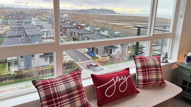Une vue depuis une fenêtre, avec un banc et des coussins, donnant sur un quartier résidentiel avec des maisons et une route.