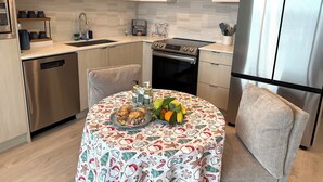 Une cuisine moderne équipée d’appareils électroménagers en acier inoxydable, une table à manger recouverte d’une nappe festive et un panier de fruits.