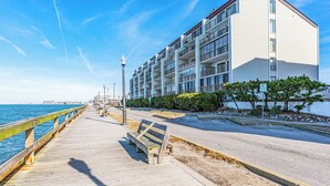 A coastal walkway with benches, a wooden railing, and a modern building with balconies. - Bayfront-2Bedroom-Balcony-Pool (Ocean City)