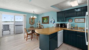 A kitchen with a wooden island, teal cabinets, and a view of the water through a sliding door. - Bayfront-2Bedroom-Balcony-Pool (Ocean City)