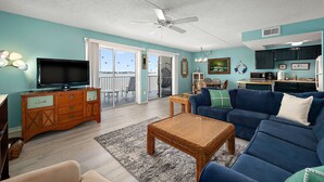 A living room with a television, sofa, and coffee table. There is a balcony with a view of the sky and birds. - Bayfront-2Bedroom-Balcony-Pool (Ocean City)