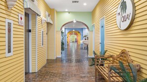 Corredor de hotel com paredes amarelas, chão de tijolos e balcão de recepção com o logotipo de uma palmeira.