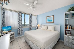 A bedroom with a bed, a TV, a bookshelf, and a window with curtains. - Ocean View 2 Bedroom-2 Bathroom (Ocean City)