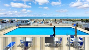Área de piscina com vista para o oceano, cercada por cadeiras de descanso e um portão.