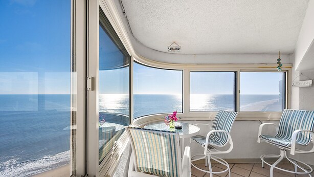 Un balcon avec vue sur l’océan, une table avec des chaises et un panneau indiquant « Sailaway ».
