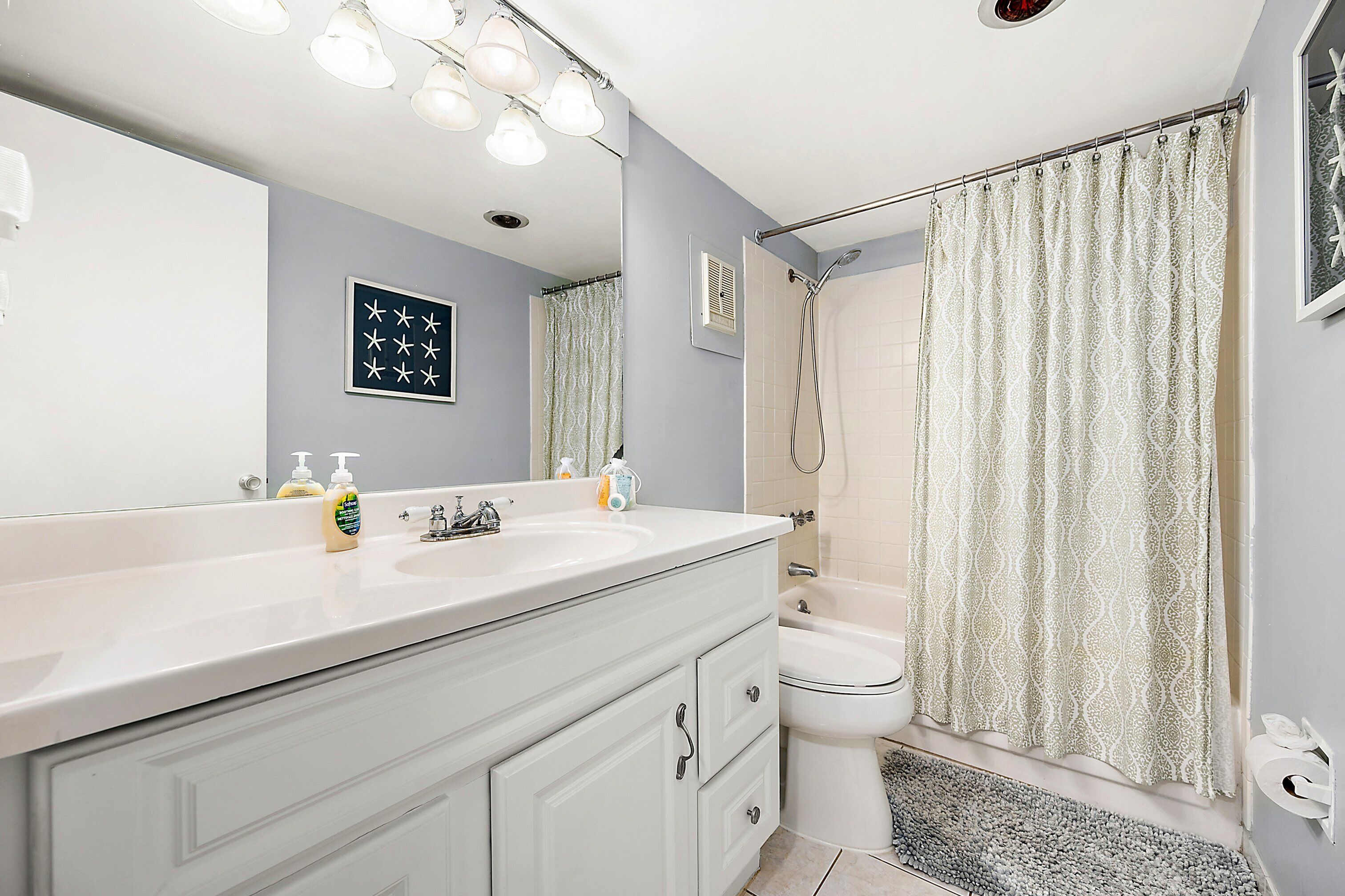 Une salle de bain avec un meuble-lavabo blanc, un grand miroir, un rideau de douche et des toilettes.