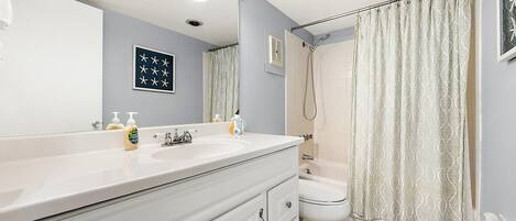 Une salle de bain avec un meuble-lavabo blanc, un grand miroir, un rideau de douche et des toilettes.