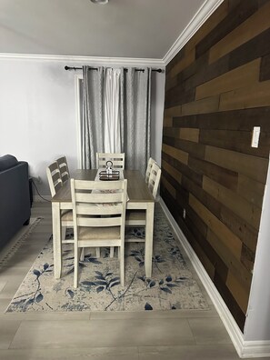 A dining area with a wooden table and chairs, a patterned rug, and a wall with a wooden panel design. - Cozy & Stylish 3-Bedroom for Families & Friends (Mount Pearl)