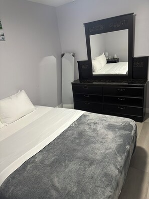 A bedroom with a bed, a dresser, a mirror, and a floor lamp. - Cozy & Stylish 3-Bedroom for Families & Friends (Mount Pearl)