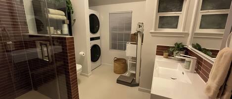 A compact bathroom with a glass shower enclosure, a washing machine, and a sink with a mirror.