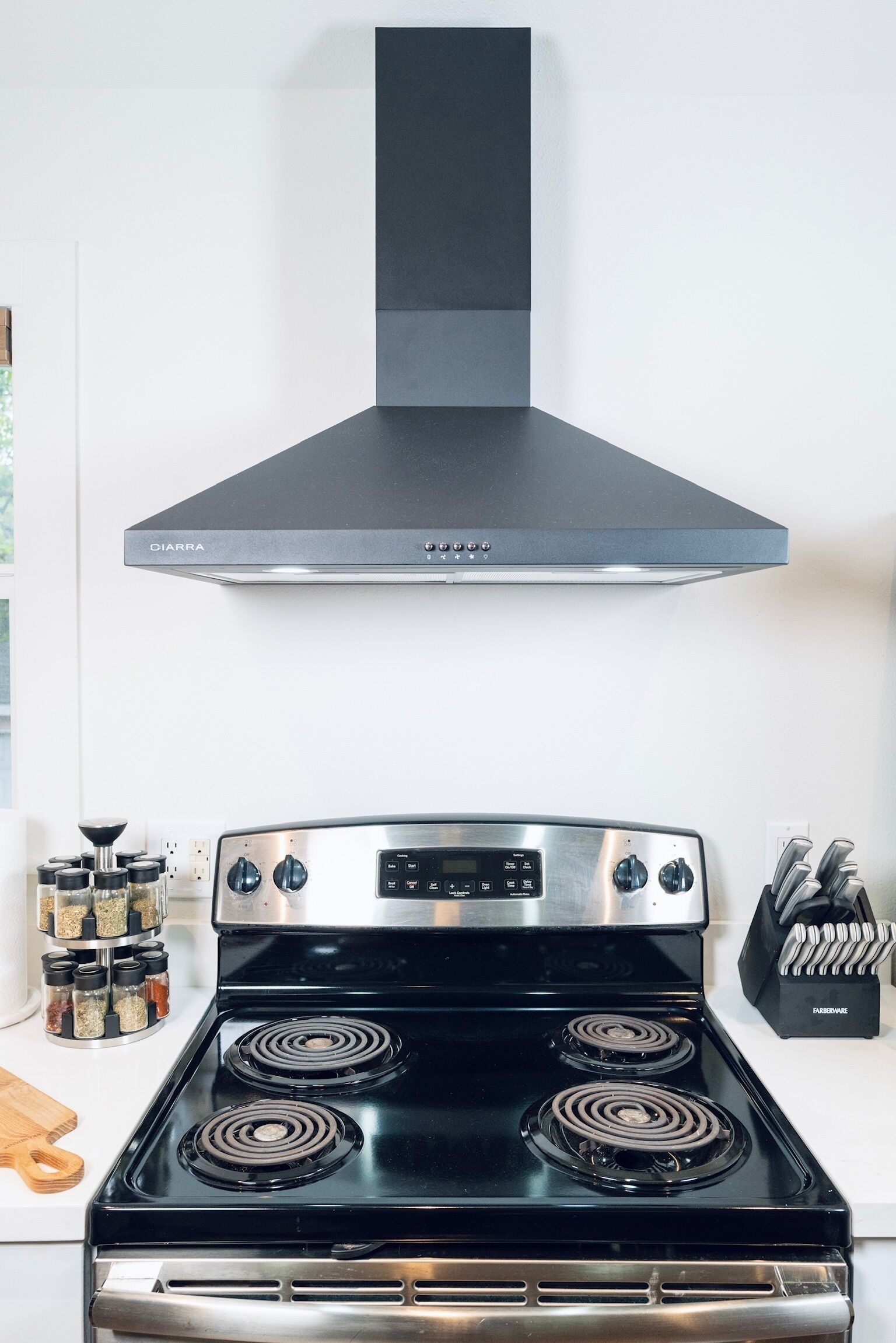 A kitchen with a black stove, a DIARRA hood, and a spice rack.