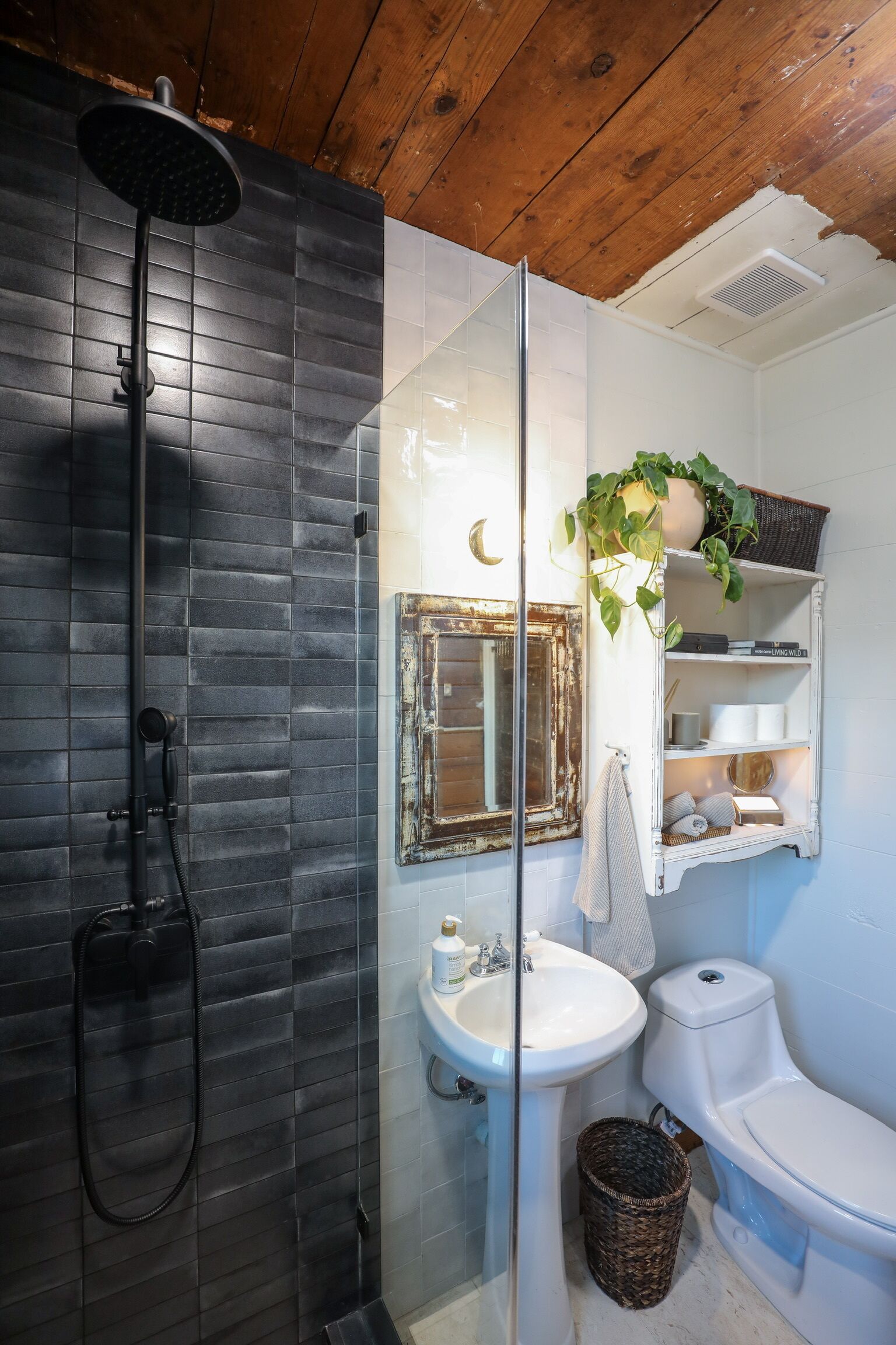 Une salle de bain avec une douche à parois de verre, un lavabo blanc, des toilettes et un miroir doté d’un cadre rustique.