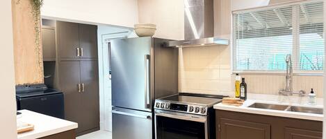 A modern kitchen with stainless steel appliances, wooden cabinets, and a large window with blinds.