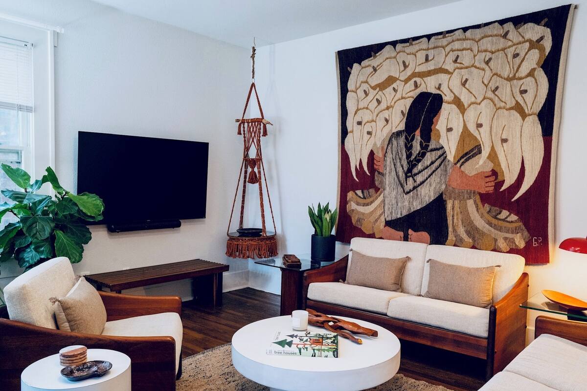 Un salon moderne avec un grand téléviseur à écran plat, un canapé en bois, une table basse ronde et une grande tapisserie.