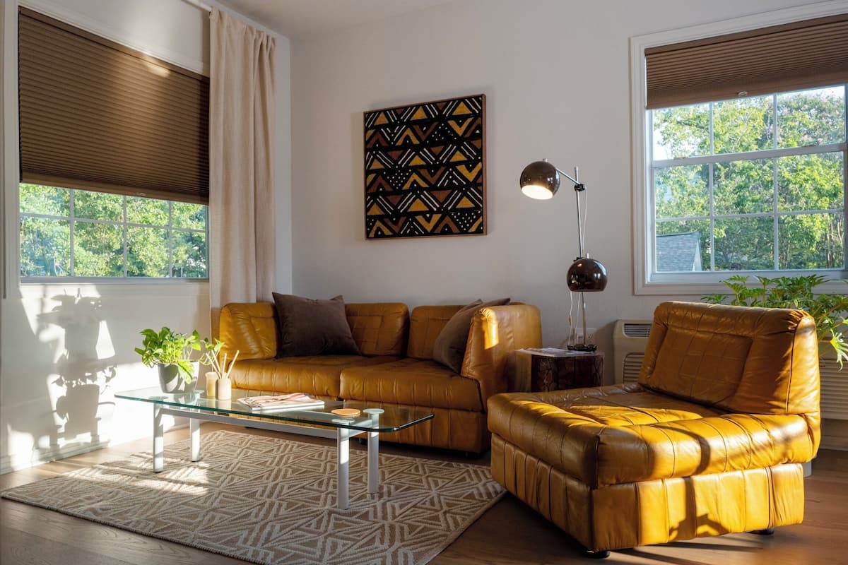 Un salon avec un canapé en cuir marron, une table basse en verre et une décoration murale à motifs.