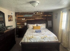 Een slaapkamer met een houten hoofdbord, een bed met bloemenbeddengoed, een nachtkastje en een bijzettafeltje.