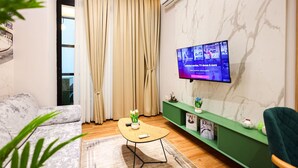 Ett modernt vardagsrum med en soffa, ett soffbord, en TV som är monterad på väggen, ett grönt konsolbord och ett fönster med gardiner.