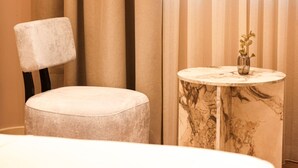 A modern bathroom with a round marble table, a cushioned chair, and a vase with a plant. - Zins Luxury Room Vollga (Durrës)